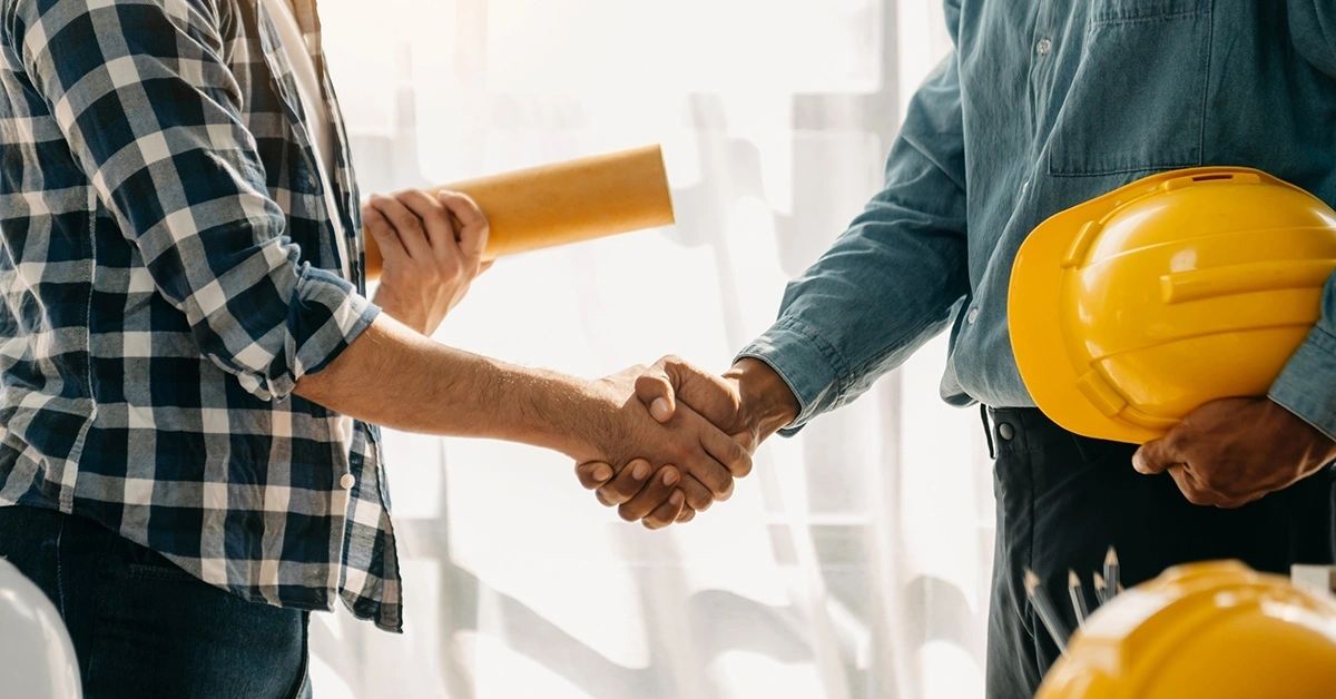 Contractor and homeowner handshake with hard hat and project plans