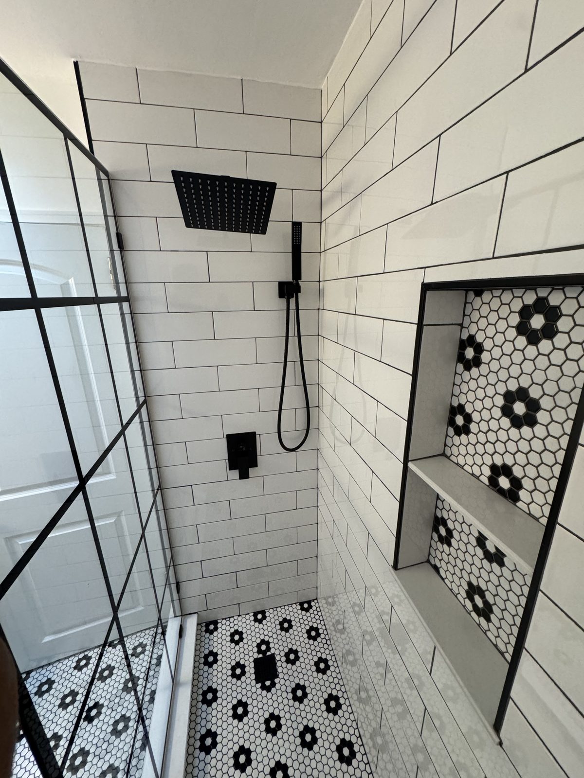 Overhead view of walk-in shower showing matte black rain showerhead, subway tile walls, and hexagonal niche detail