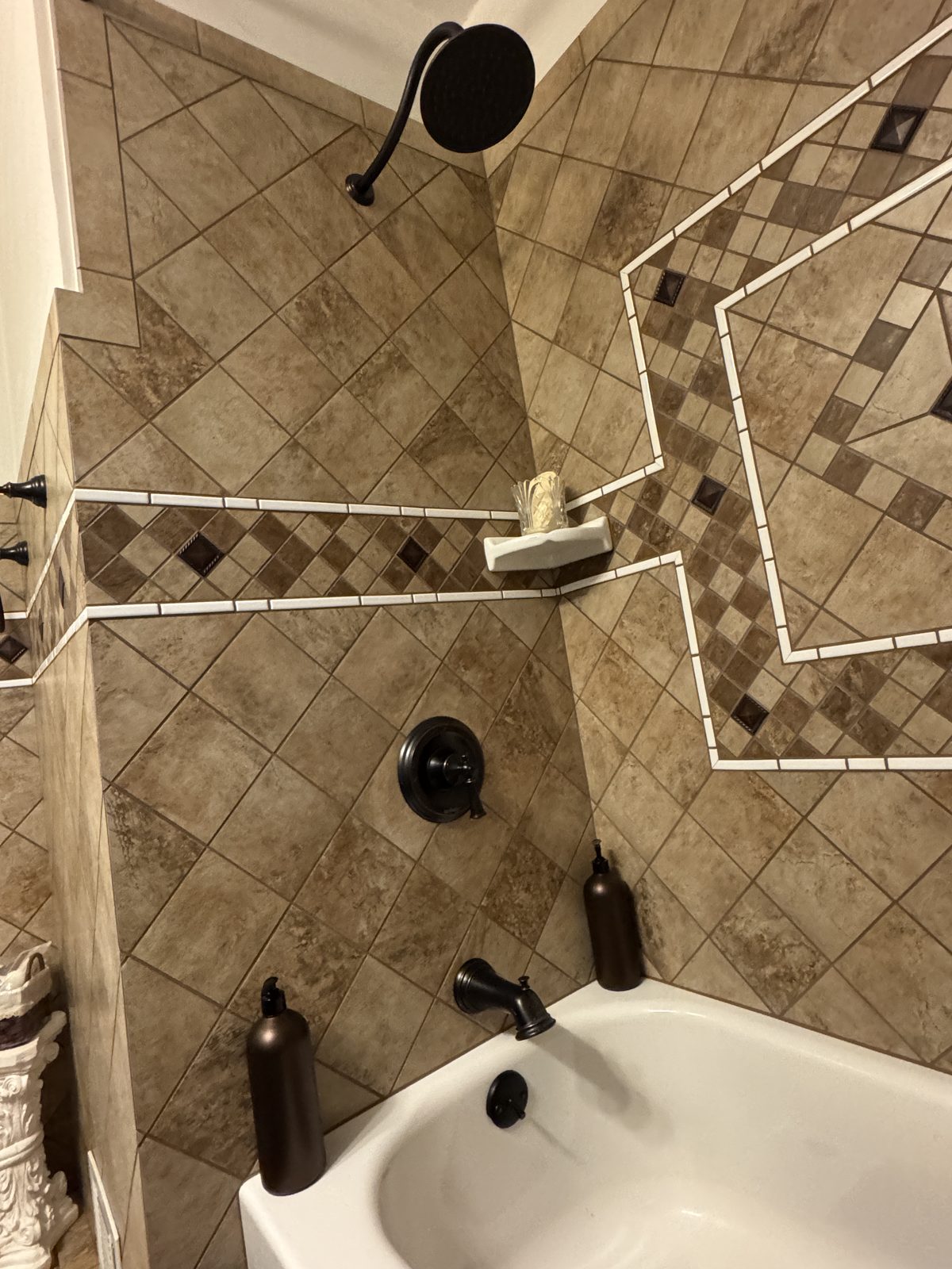 Tiled shower with diagonal brown stone tile pattern, decorative diamond border, and oil-rubbed bronze fixtures