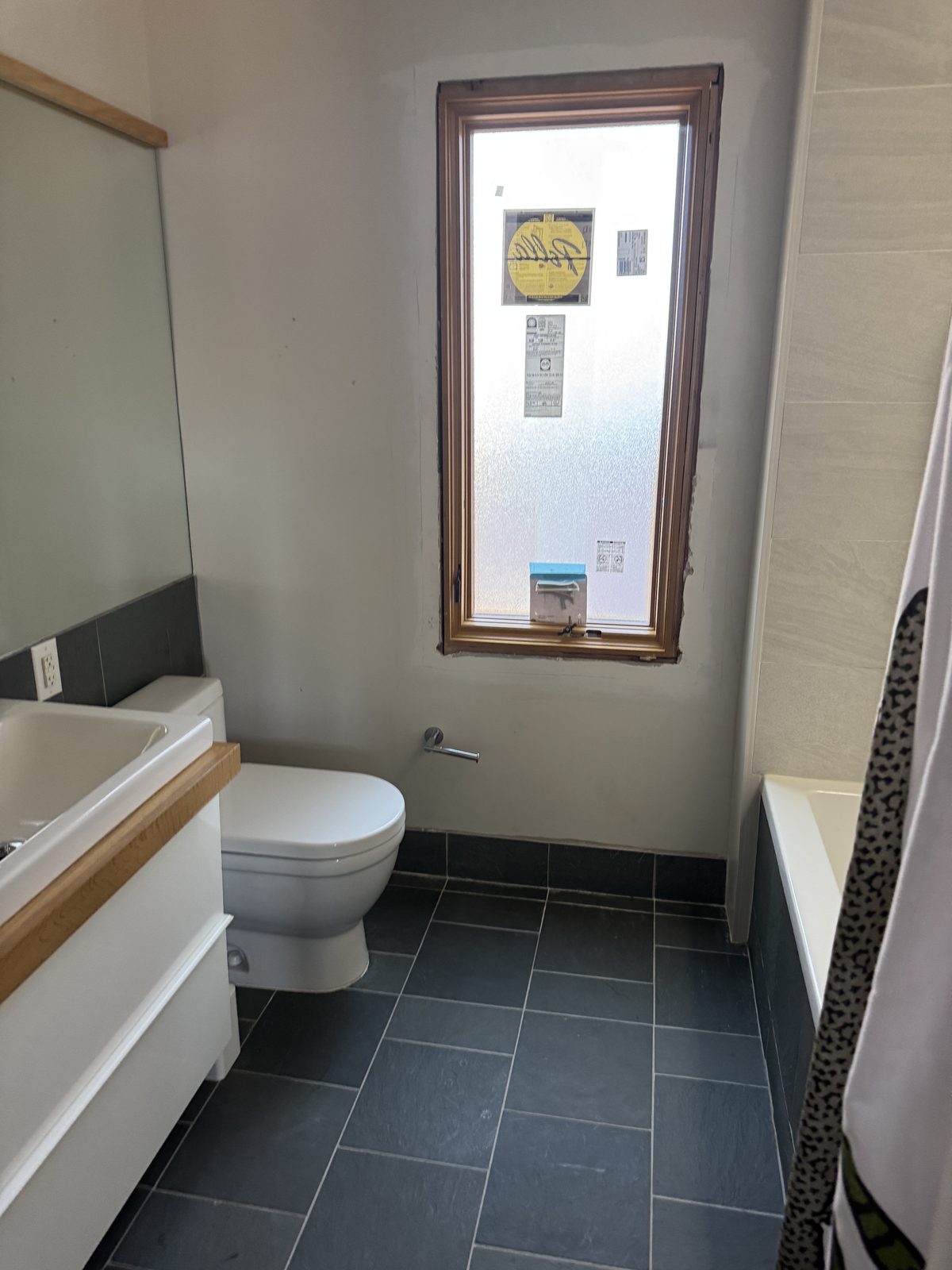 Bathroom renovation with dark slate tile surround, white vanity, new frosted window, and tub-shower combination