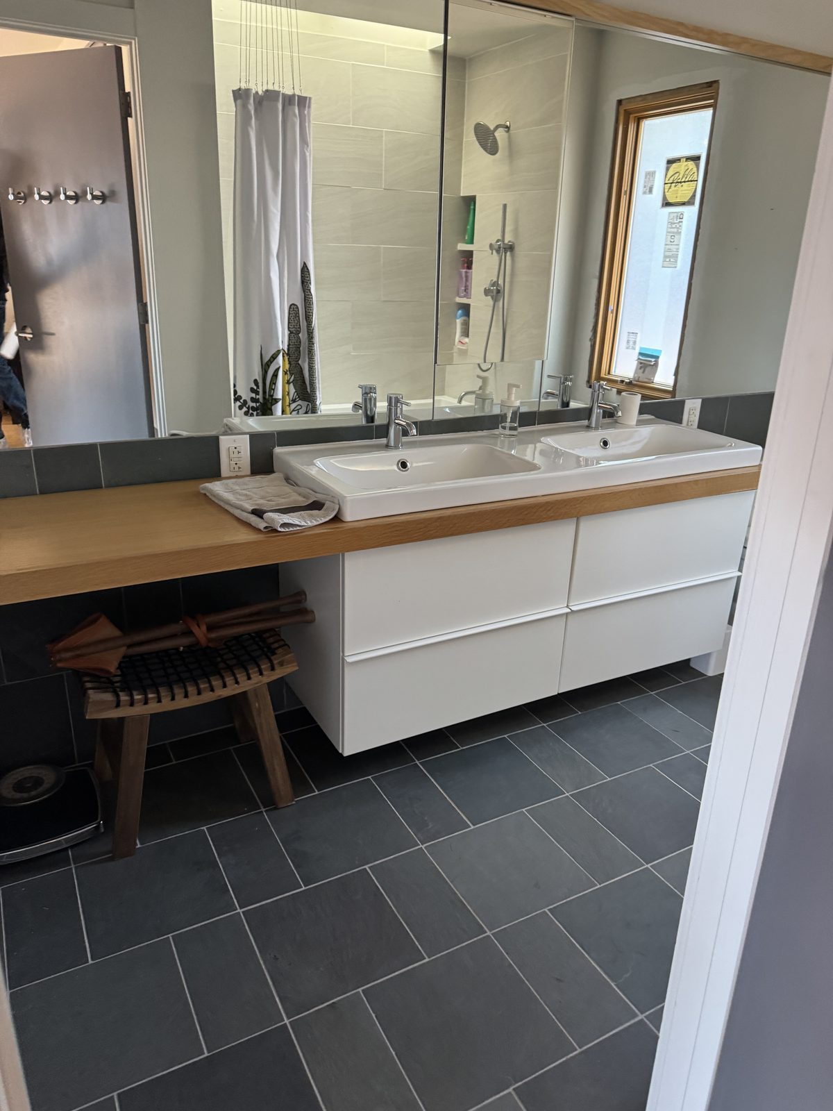 Renovated bathroom with dark slate tile, white floating vanity with mirror, tub-shower combo, and frosted window