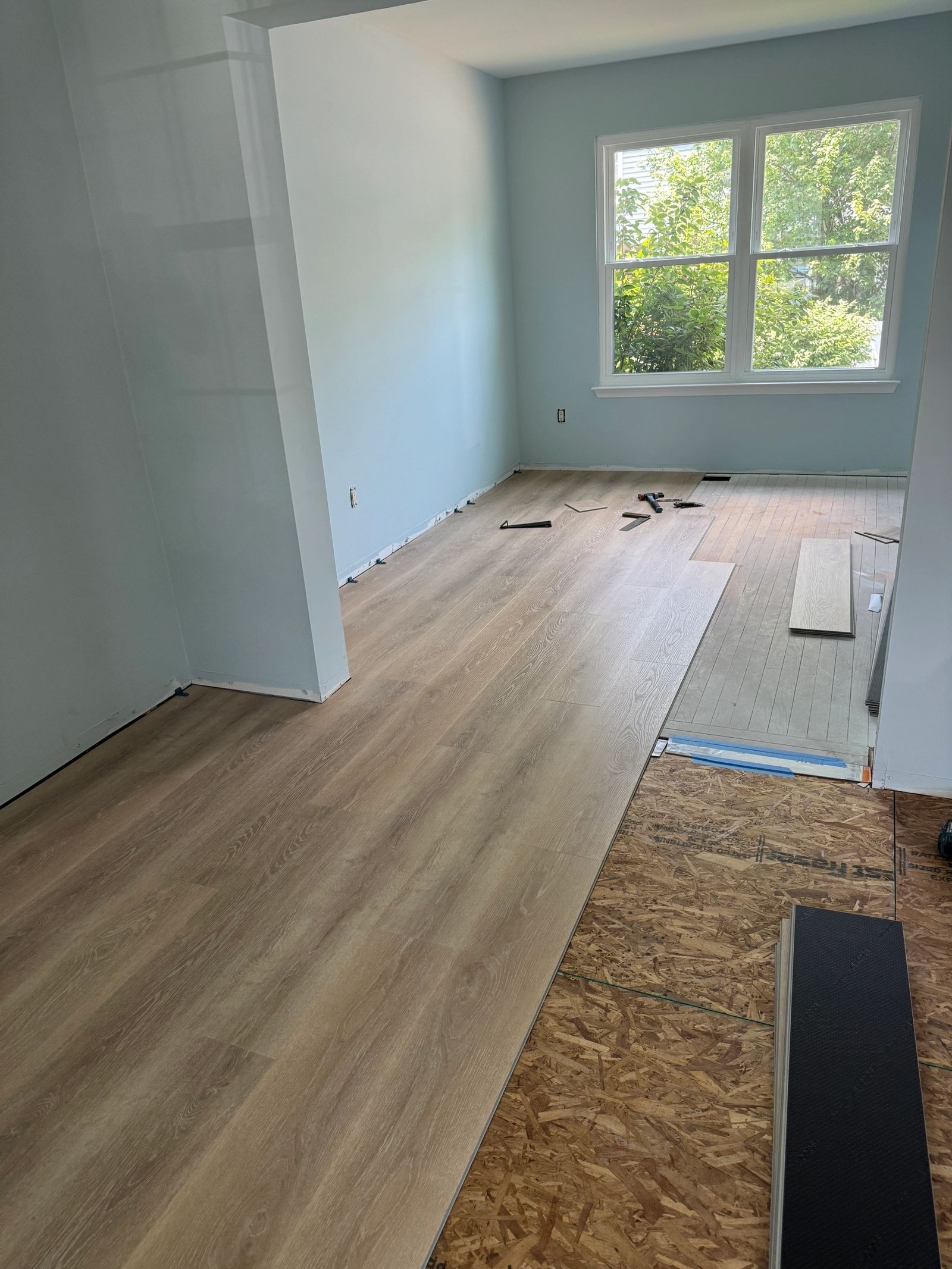 Luxury vinyl plank flooring being installed in room showing subfloor and progress