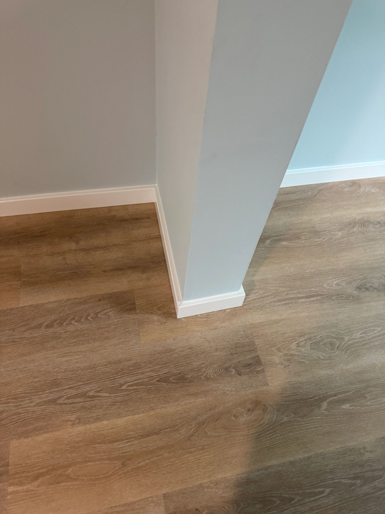 Detail of LVP flooring installed around wall corner with clean baseboard trim