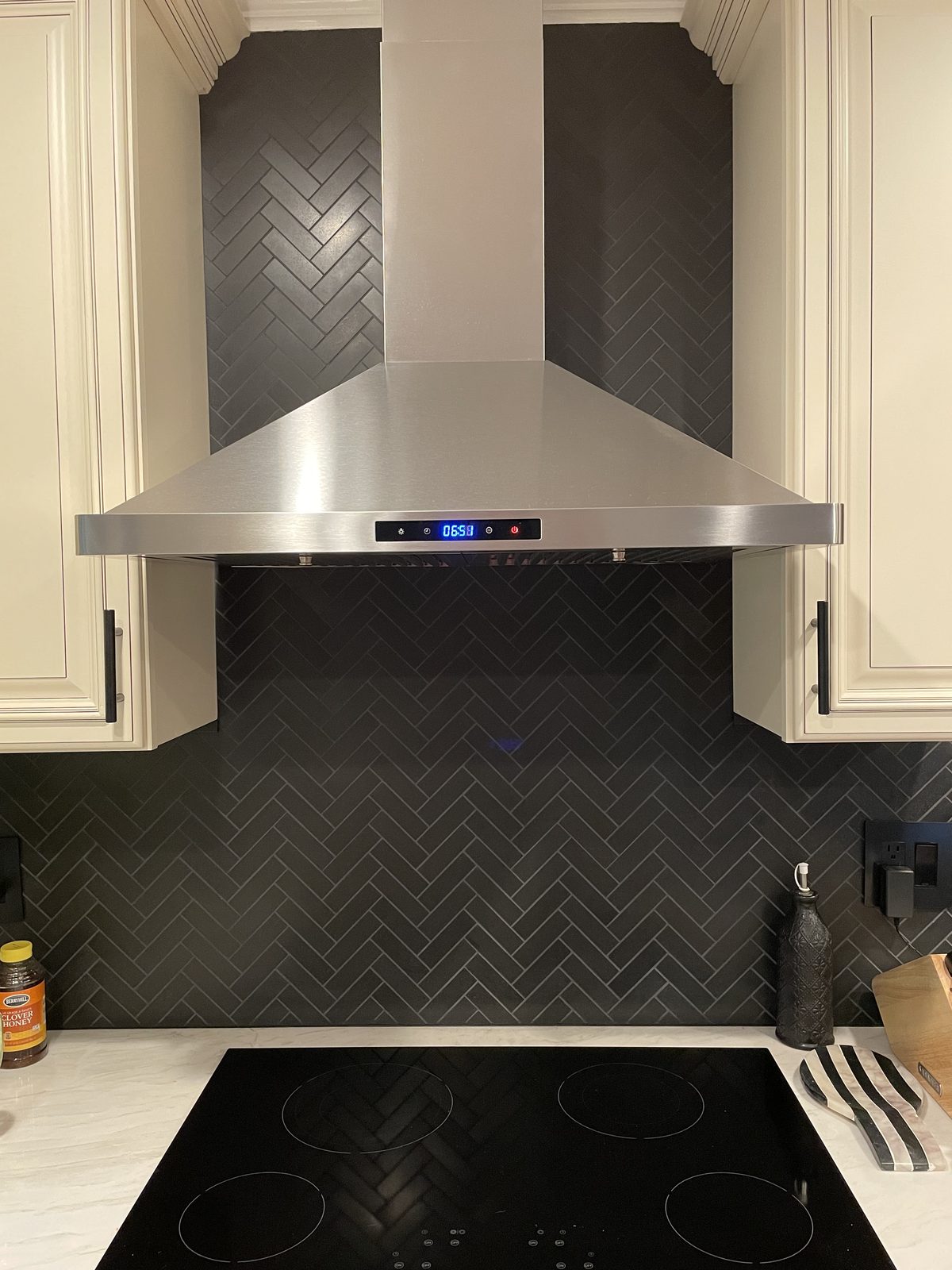 Kitchen with black herringbone tile backsplash, stainless hood, and induction cooktop