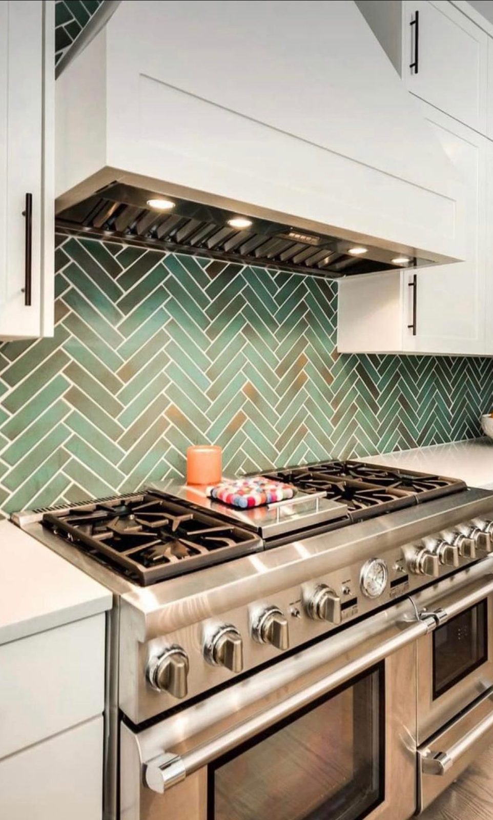 Professional gas range with green herringbone tile backsplash and custom hood