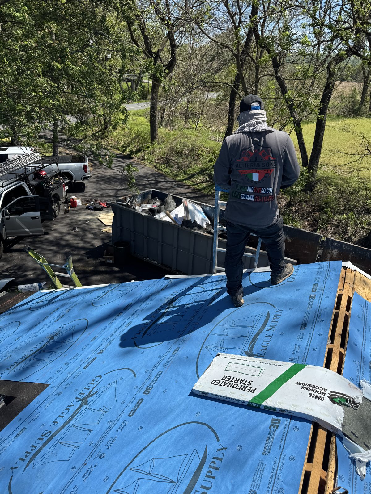 Altieri and Sons crew member on ladder installing synthetic underlayment on roof with branded company shirt