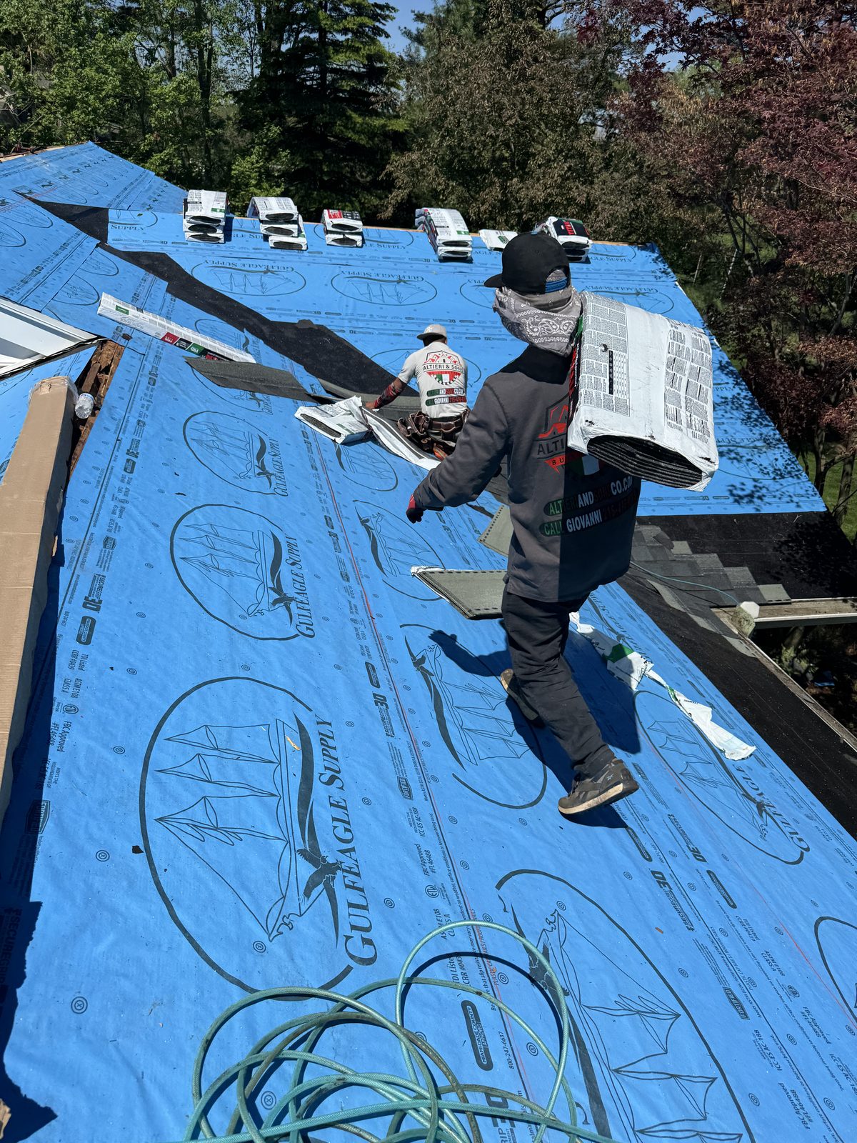 Roofing crew member staging shingle bundles on roof covered with blue GulfEagle Supply synthetic underlayment