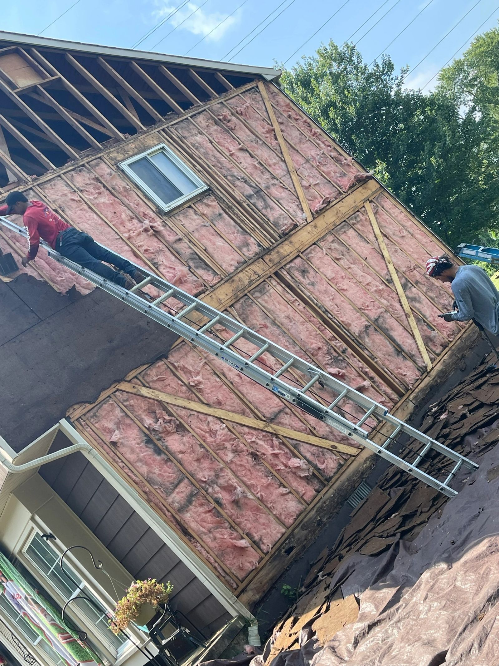 Crew removing old siding to expose insulation and framing for replacement