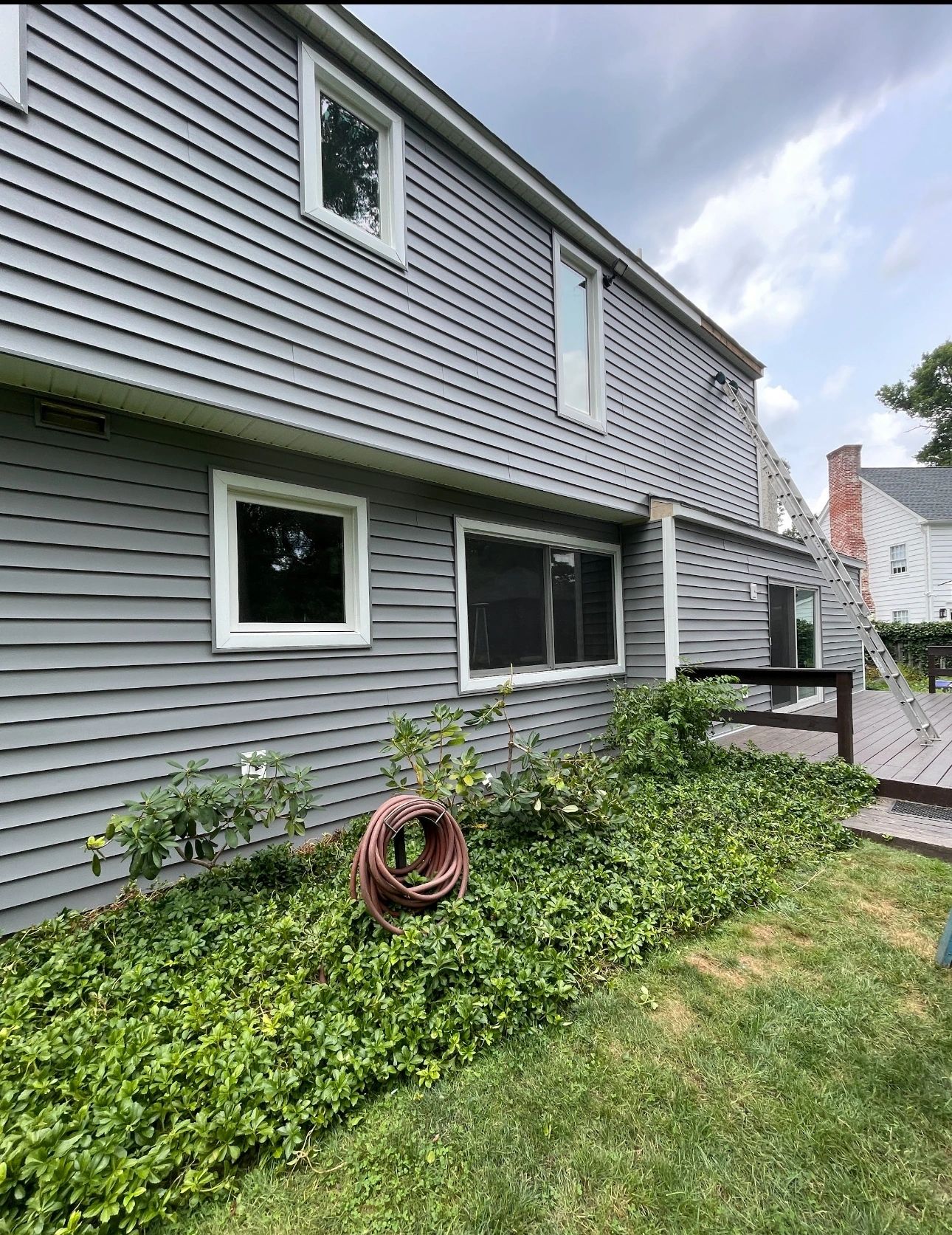 Completed gray vinyl siding on two-story home rear view with landscaping