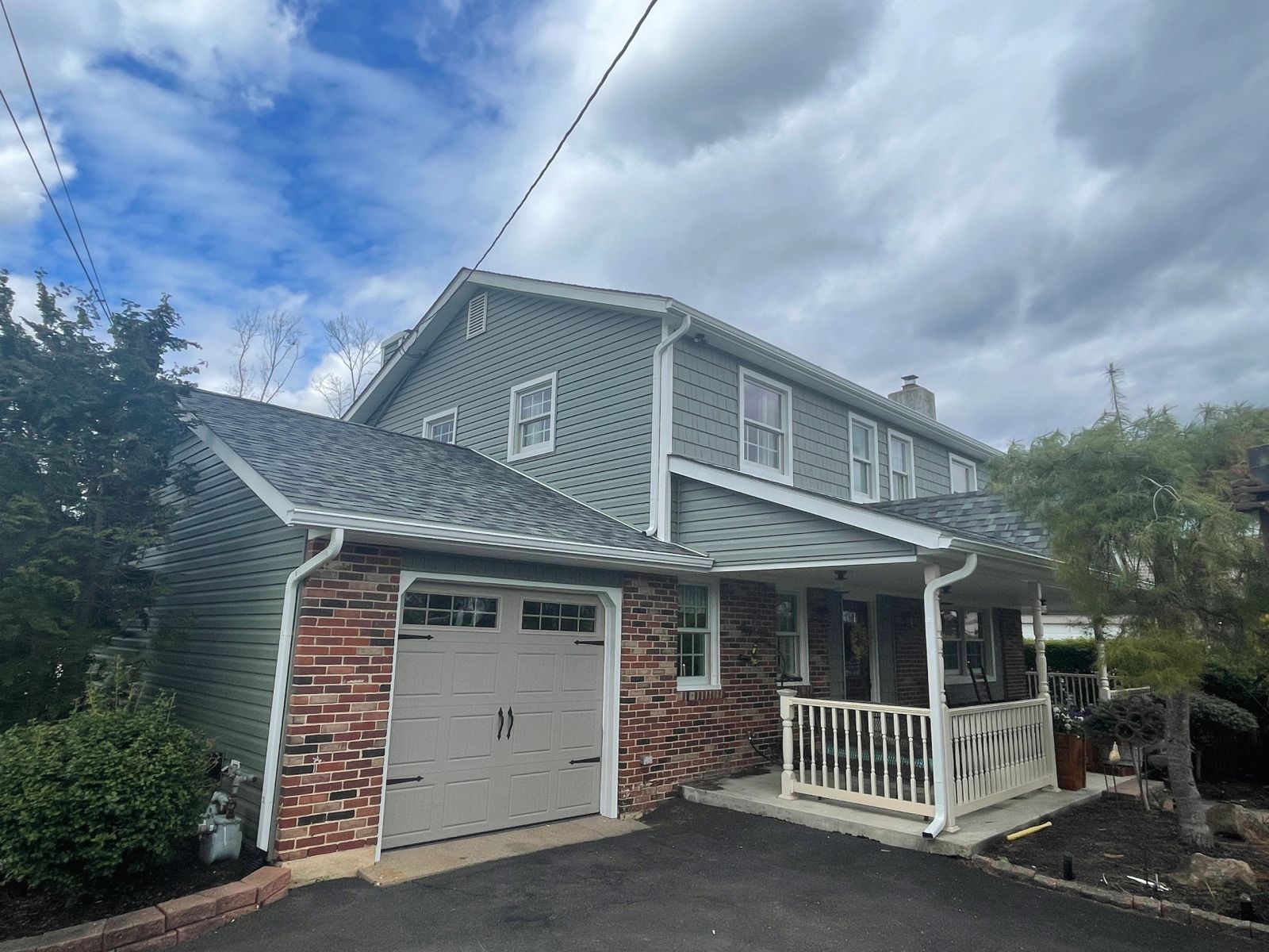 Two-story home with completed green-gray siding, front porch, and new garage door