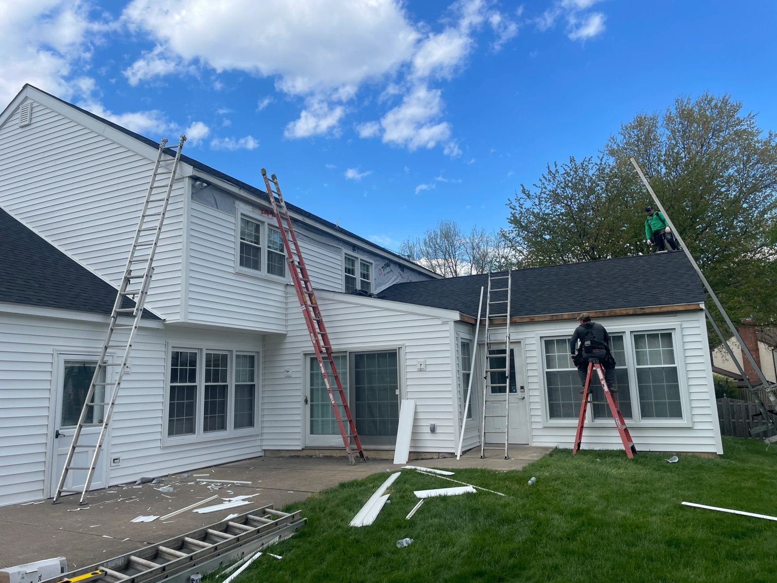 Crew installing white vinyl siding on rear of two-story home with ladders